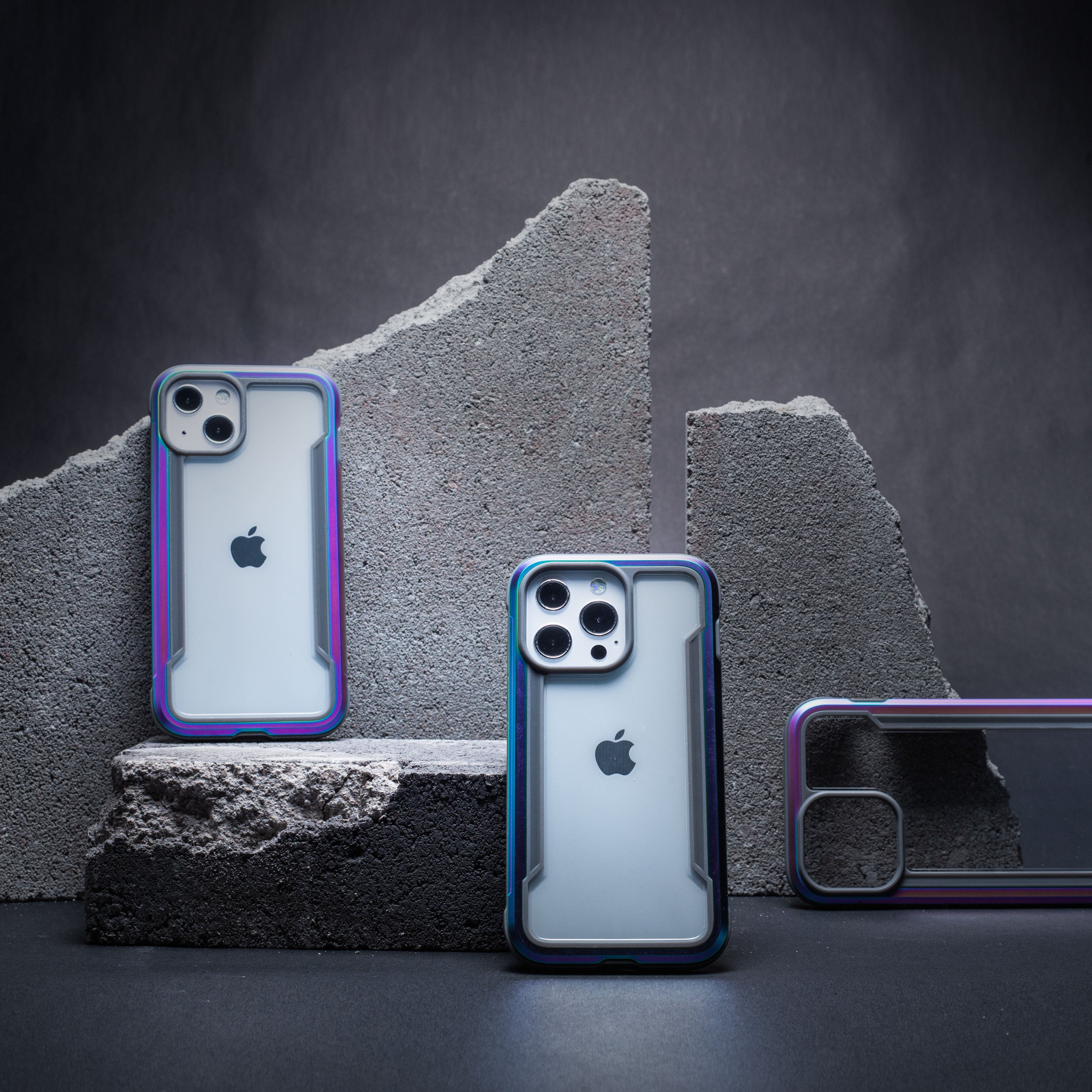 Three Raptic iPhone 13 Case - SHIELD PRO cases sitting on top of a stone wall, offering drop protection.