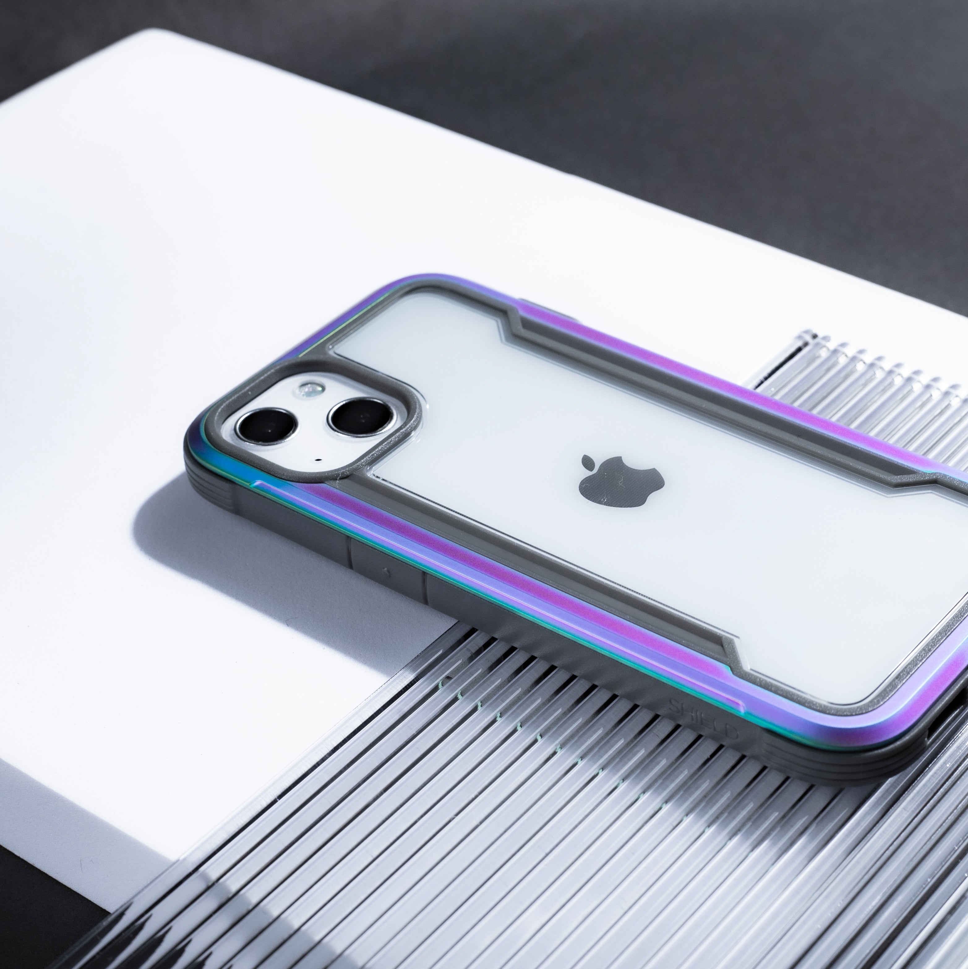 The iPhone 13 Case - SHIELD PRO by Raptic is sitting on top of a table, providing drop protection.