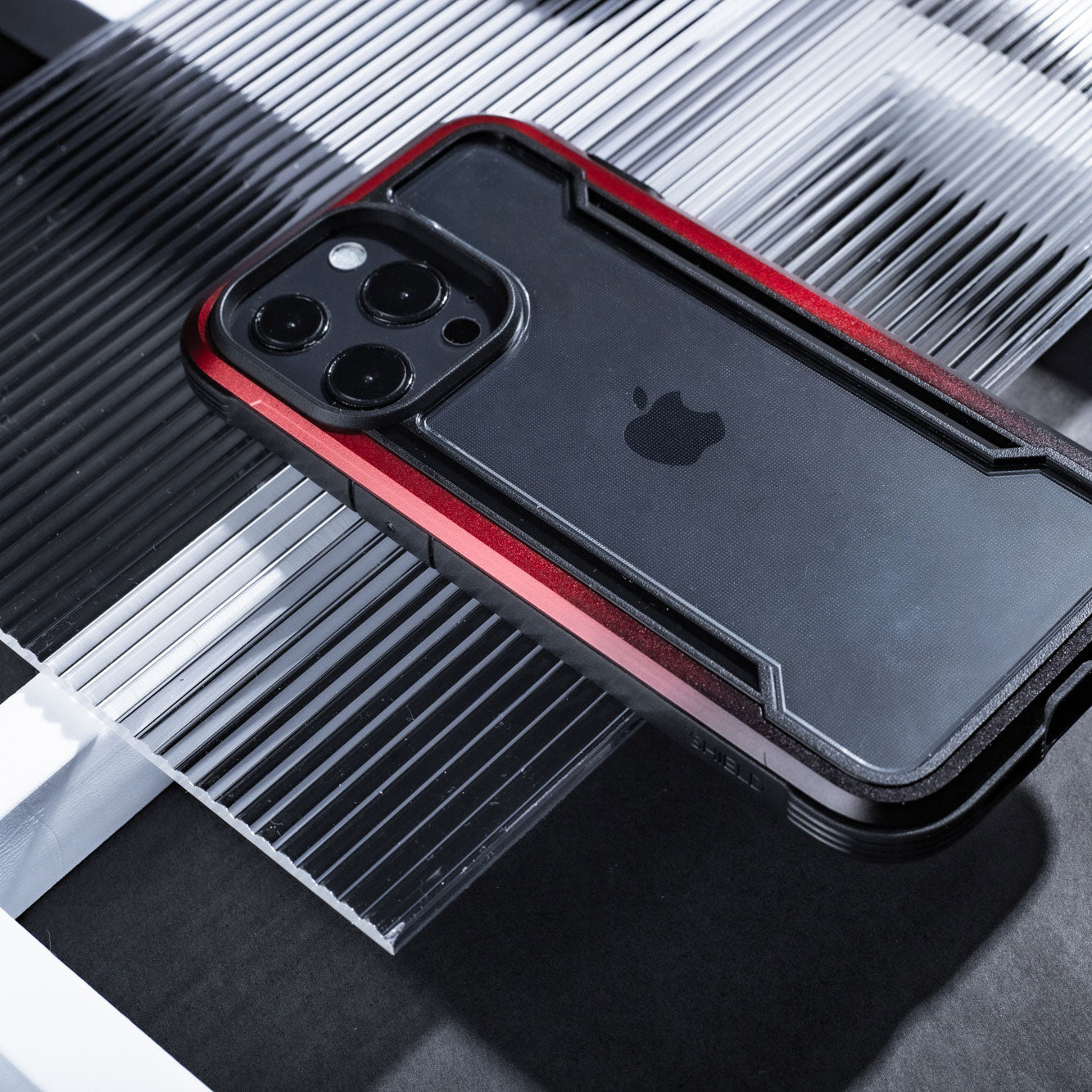 A red and black iPhone 13 Case - SHIELD PRO by Raptic with drop protection on top of a glass table.