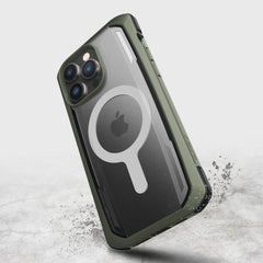 The iPhone 14 Pro Max Case ~ Secure by Raptic is a green rugged case with a translucent back featuring a circular MagSafe design. Made from biodegradable materials, it provides military-grade drop protection and is captured mid-air against a light background.