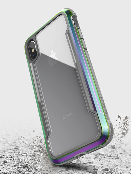 A smartphone with a Raptic iPhone X/XS Shield case in metallic green and purple floats above a textured surface, highlighting its military-grade drop protection.