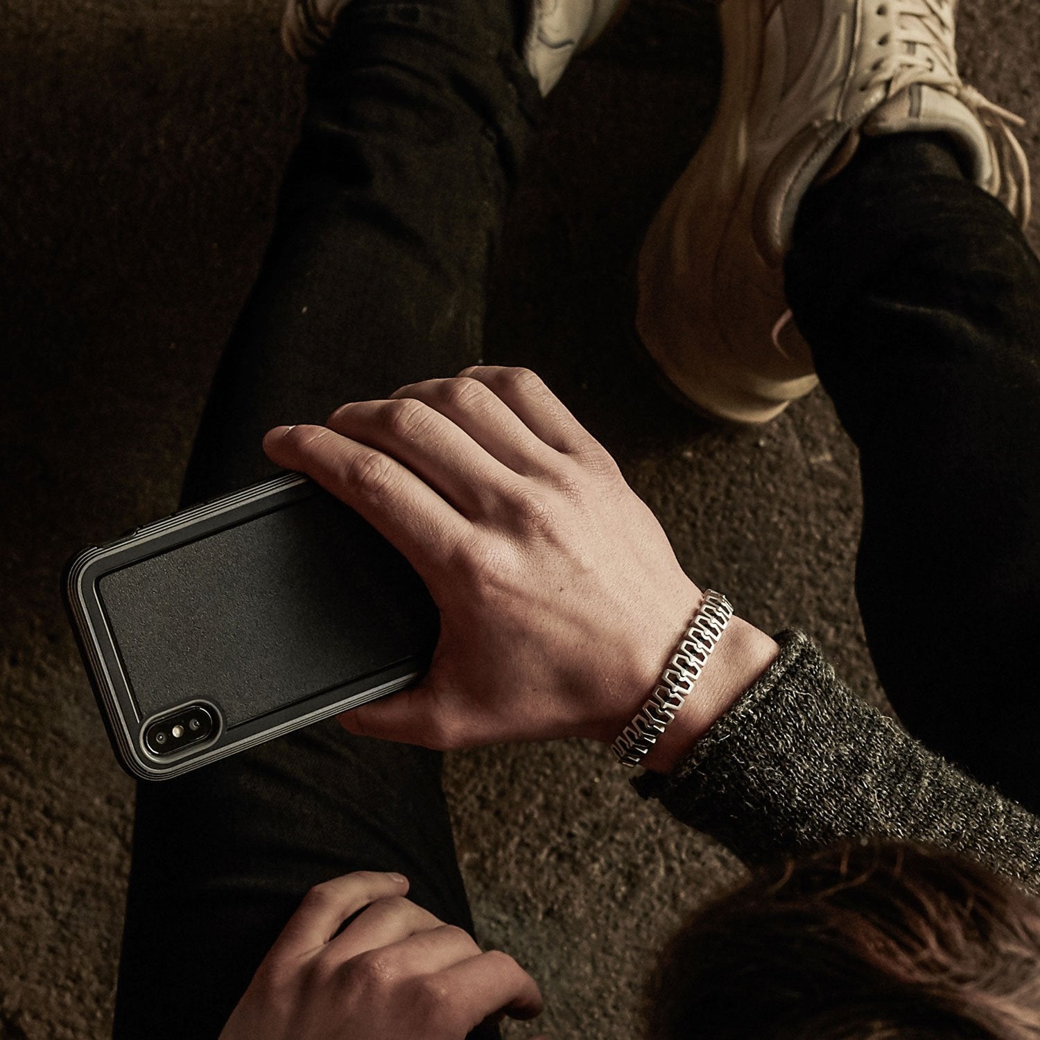 A person sitting on the ground, holding an iPhone XR adorned with a Raptic ULTRA case for superior device protection.