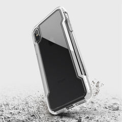 The Raptic iPhone XS Max Case - CLEAR, featuring transparent, anti-yellow, and anti-scratch protection, appears suspended above a cracked surface to demonstrate its military-grade drop protection.
