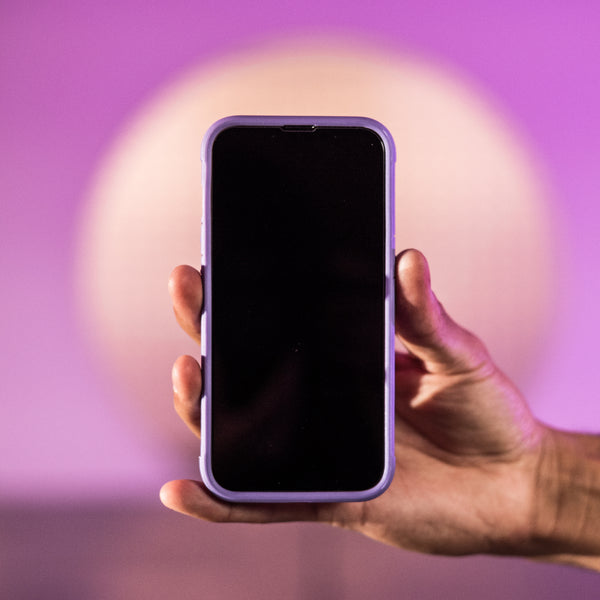 A hand holding up a Raptic TERRAIN iPhone 13 Case with a purple background.