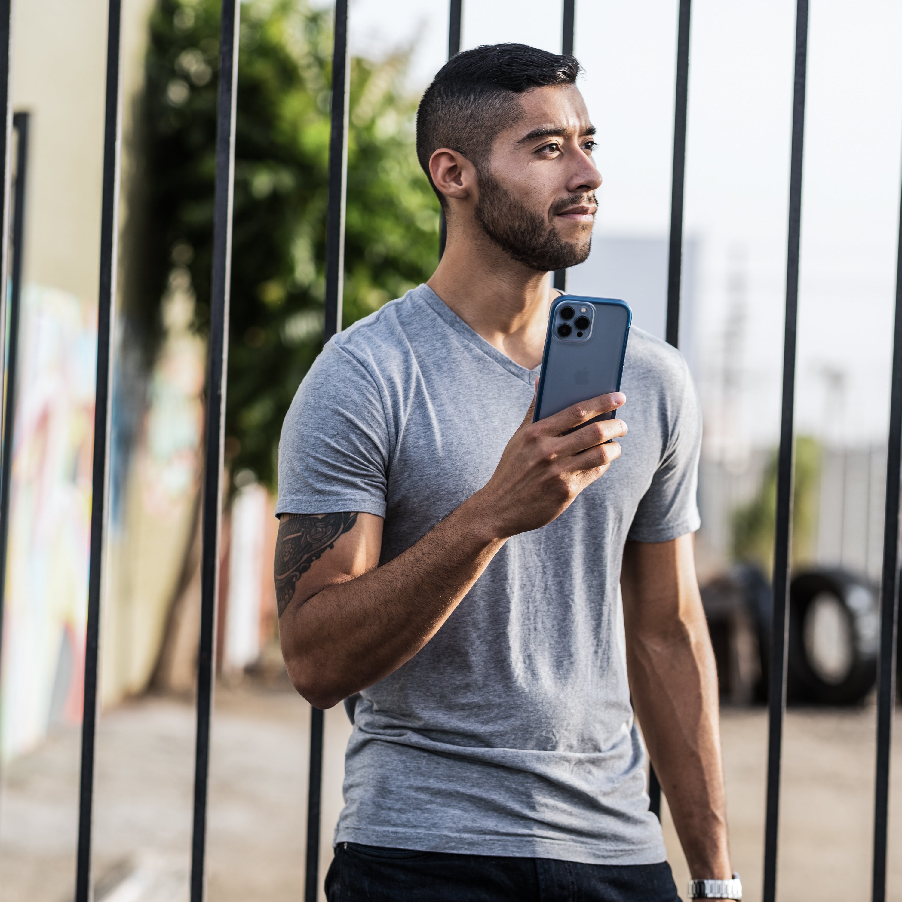An eco-friendly man holding an iPhone 13 Case - TERRAIN by Raptic in front of a fence.