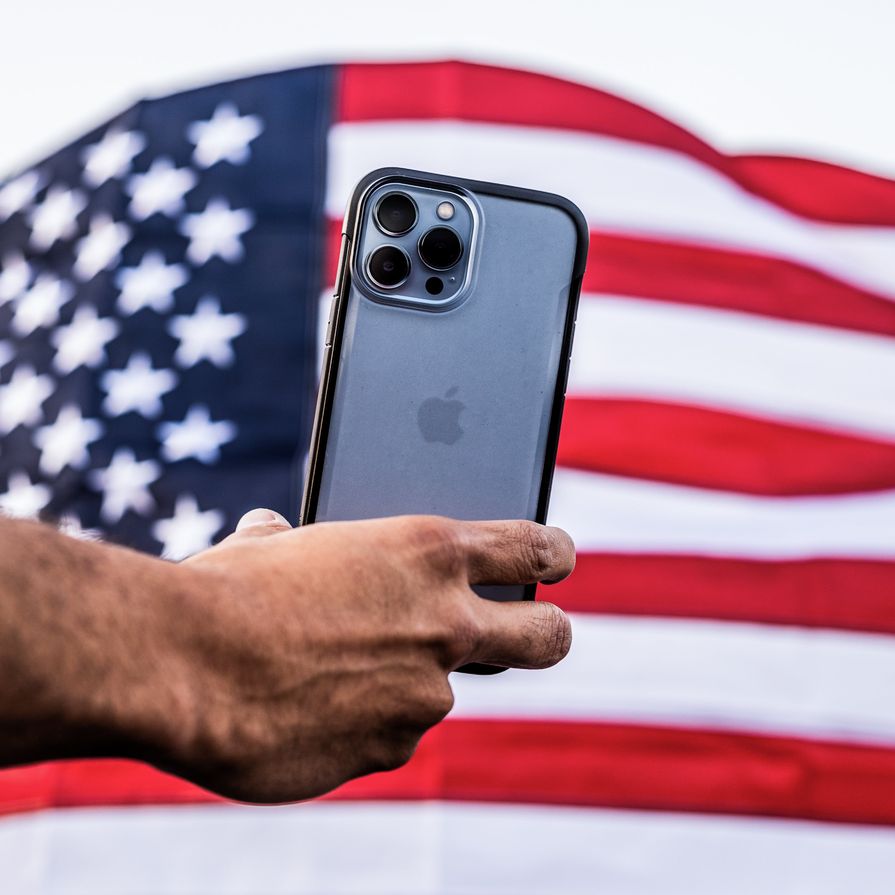 A person proudly showcasing their eco-friendly Raptic iPhone 13 Pro Case - TERRAIN in front of an American flag.