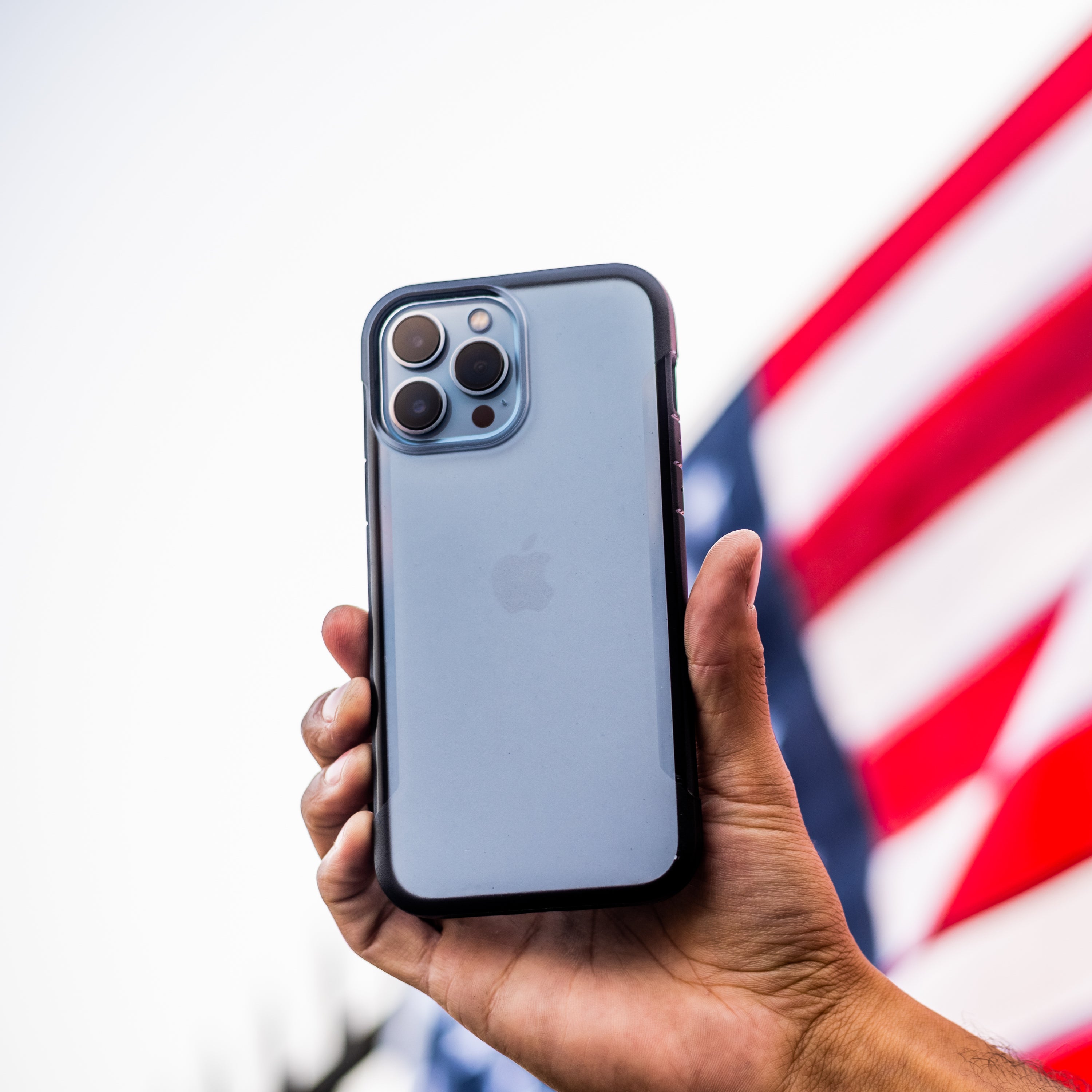 A person holding a Raptic iPhone 13 Pro Max Case - TERRAIN in front of an eco-friendly American flag.